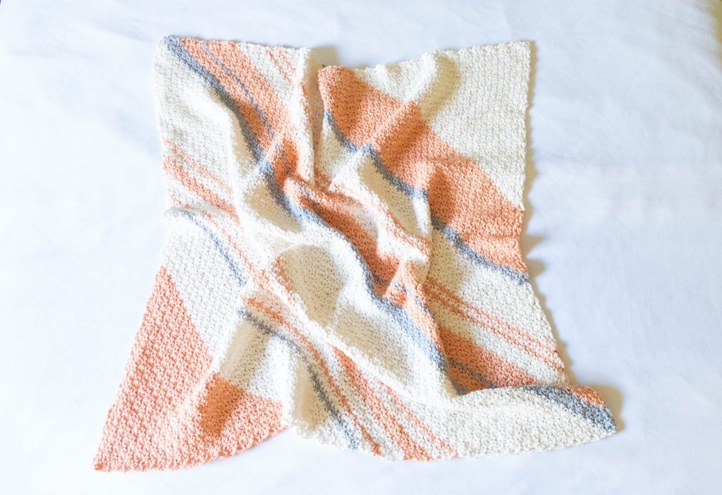 striped baby blanket done in corner to corner crochet with cream, grey, and peach stripes.