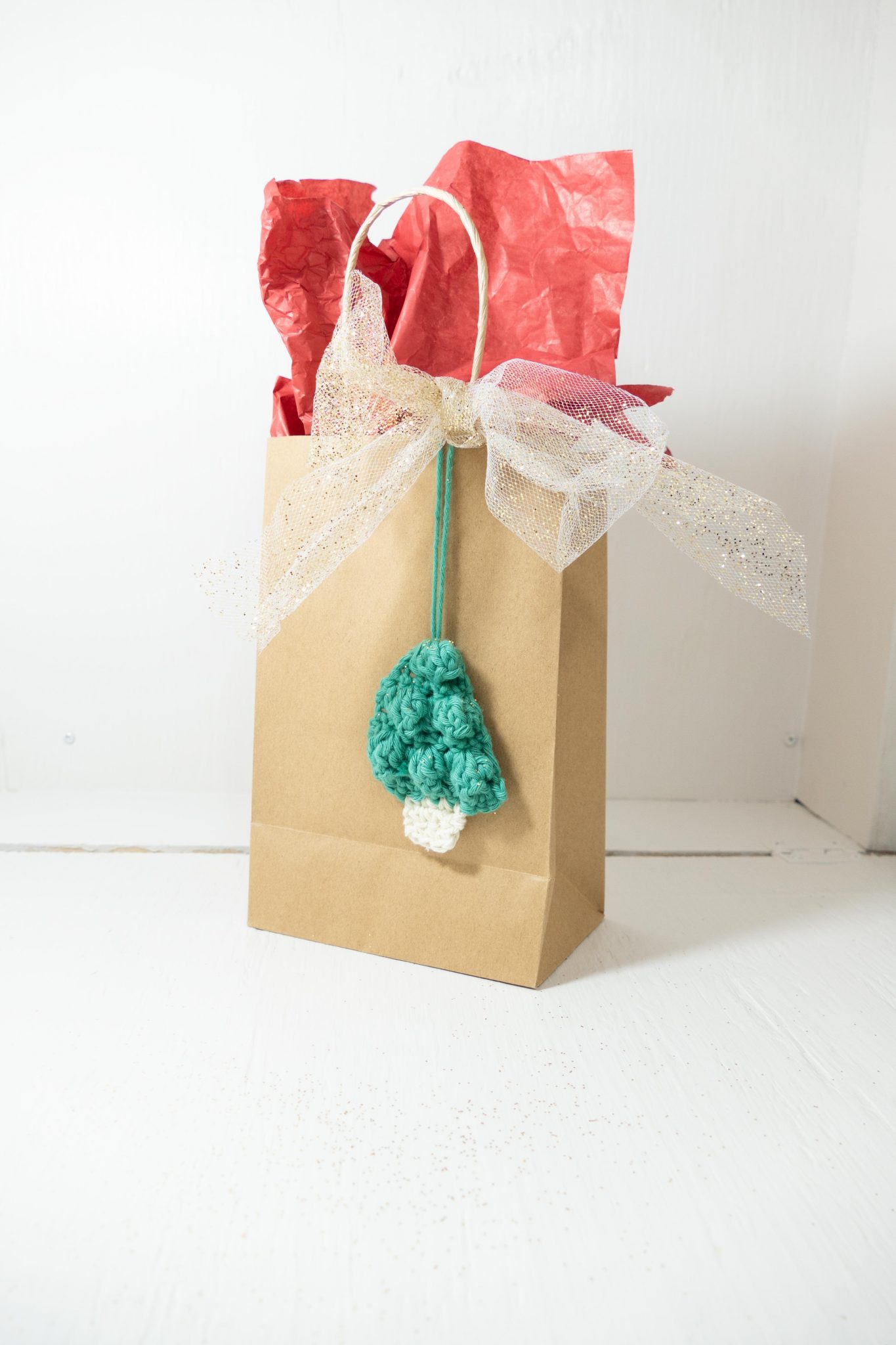The small green crochet tree hangs on the outside of a plain gift bag for decoration