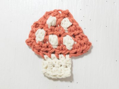 Flatlay image of a small pink and white crochet mushroom