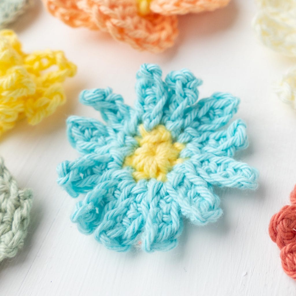 flatlay of crochet flowers, focusing on a blue diasy design