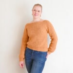 amelia stands against a light colored wall modeling the textured turnover crochet sweater.