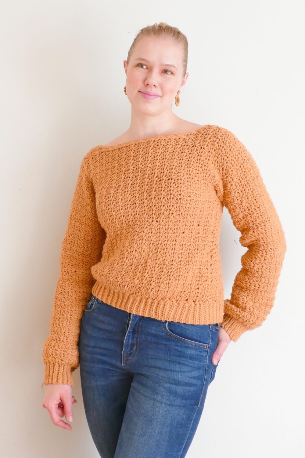 amelia stands against a light colored wall modeling the textured turnover crochet sweater.